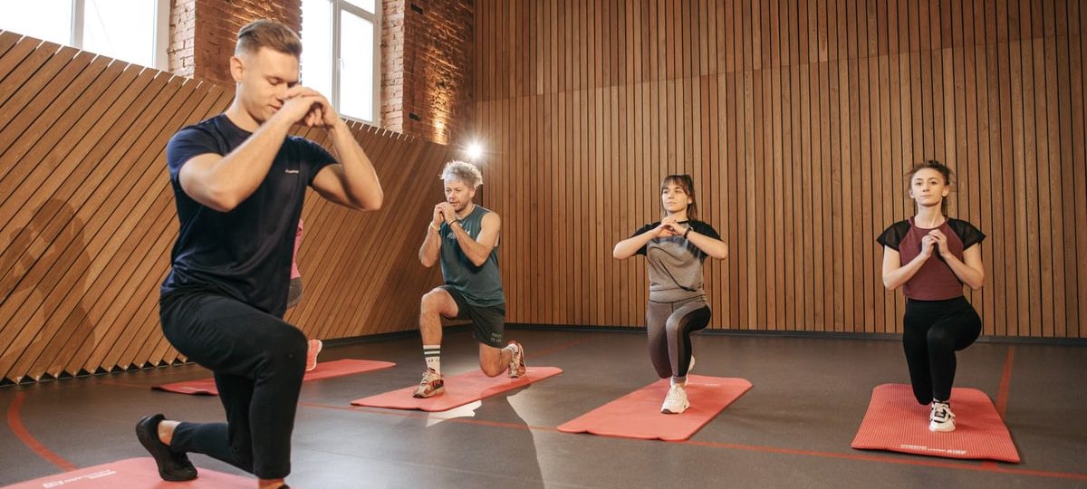 Adults practicing exercises on yoga mats in a contemporary studio setting.